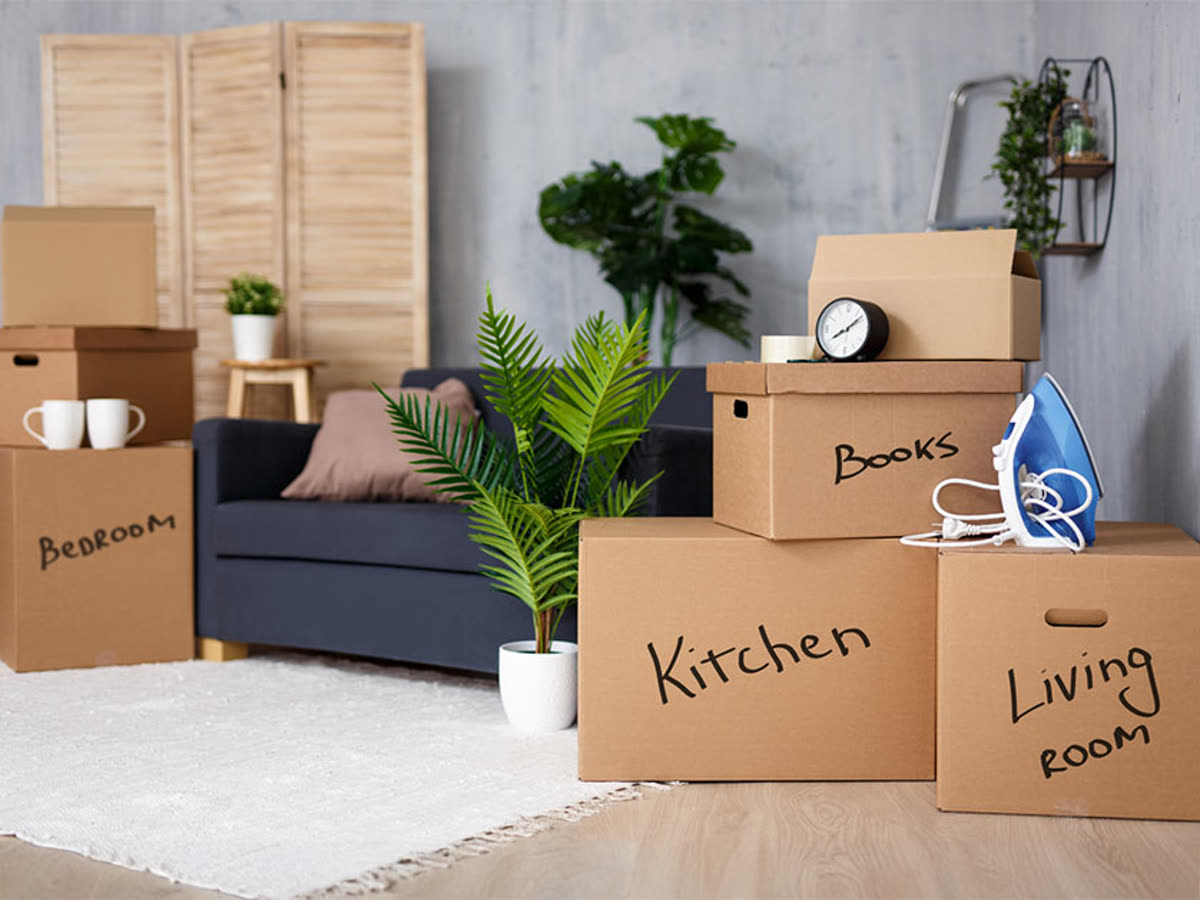 Moving boxes clearly labeled by room — bedroom, kitchen, living room, and books — in a family's living room