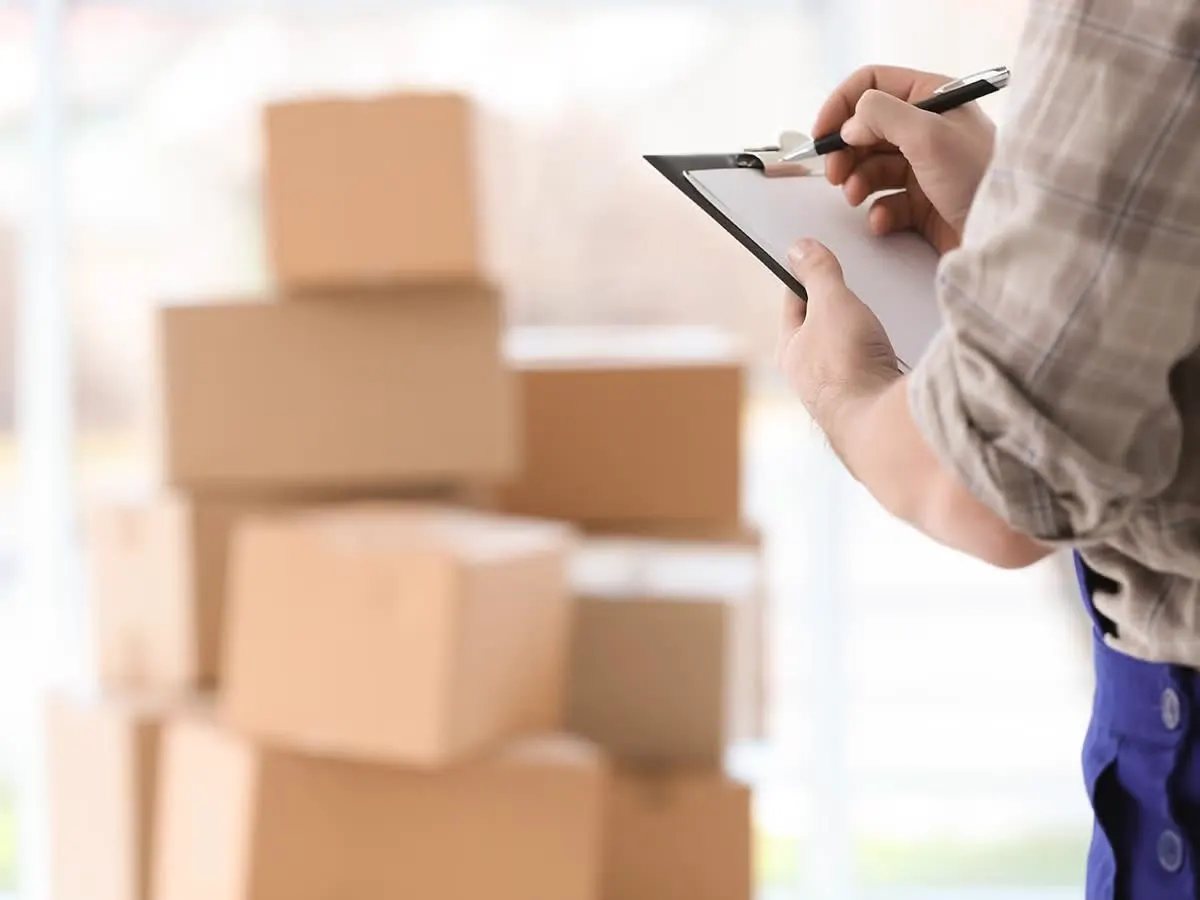 A moving professional checking off items on a clipboard checklist beside stacked boxes